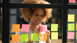 African woman writing down on sticky notes view through glass